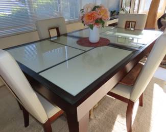 Modern dining table with glass inlaid, four matching chairs with cut outs and an extra leaf.