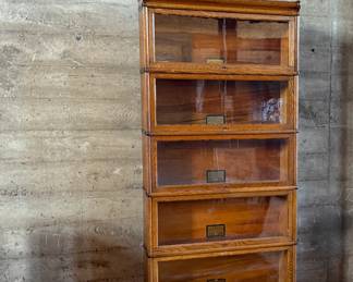 This lot features a stacking barrister bookcase manufactured by Globe Wernicke, dating back to the early 1900s. This bookcase in particular has a total of seven (7) pieces – 5 stacking bookcases, a base, and a topper. This piece measures from top to bottom, 79” H x 34” W x 11.5” D.

