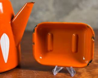 This lot features a vintage Cathrineholm Lotus coffee pot or kettle in orange enamel, accompanied by two matching orange enamel soap dishes. 


