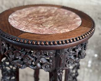 This lot features an antique Chinese carved rosewood marble-top plant stand that measures, 32” H x 13.5” W x 13.5” D. It features intricate carvings of leaf and floral motifs on the frieze, apron, and legs. These stands, also known as xiangji, are often considered antique or vintage pieces, with some dating back to the Republic Period (1912-1949).


