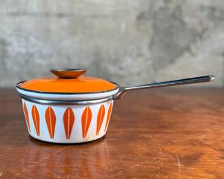 This lot features a vintage Cathrineholm Lotus enamel saucepan with a lid in an orange and white color scheme. The popular "Lotus" pattern was designed by Grete Prytz Kittelsen and produced during the early to mid-1960s in Norway.

