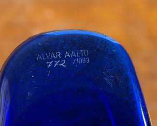 This lot features a Iittala Alvar Aalto Collection vase in ultramarine blue mouth-blown glass. It is also known as the Savoy Vase. The vase was designed by Finnish architect Alvar Aalto and his wife Aino for a design competition in 1936. It became an iconic piece of Finnish design after being displayed at the 1937 Paris World’s Fair. The unique, wavy shape was reportedly inspired by the hem of a Sami woman’s dress, with original sketches titled “The Eskimo Woman’s Leather Breeches”. Each vase is still manufactured by skilled glassblowers at the Iittala factory in Finland using original wooden molds. This vase is accompanied with Aalto’s MOMA book.

