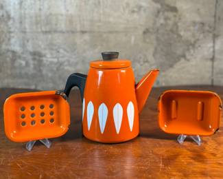 This lot features a vintage Cathrineholm Lotus coffee pot or kettle in orange enamel, accompanied by two matching orange enamel soap dishes. 

