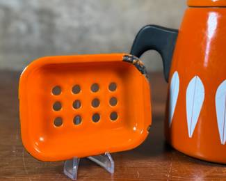 This lot features a vintage Cathrineholm Lotus coffee pot or kettle in orange enamel, accompanied by two matching orange enamel soap dishes. 


