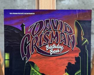 This lot features a 1996 David Grisman Quintet concert poster for a "Birthday Bash" event at The Warfield in San Francisco. The event featured the David Grisman Quintet with special guests including Vassar Clements, Peter Rowan, Herb Pederson, and John Kahn. This poster is an original print from the Bill Graham Presents series, identified by the code BGP-139 and the artwork was created by artist, Jim Phillips. This poster measures, 19” H x 13” W.

