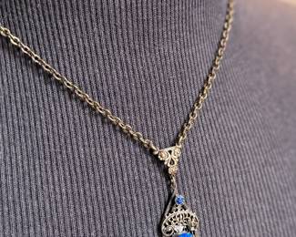 This lot features an antique Art Deco sterling silver filigree pendant necklace with a large blue central stone, likely blue chalcedony or glass, and marcasite accents. The intricate filigree design and geometric patterns are characteristic of the Art Deco period, circa the 1920s-1930s. This necklace measures, 18”.

