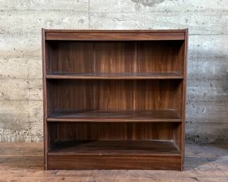 This lot features a three-shelf bookcase with a walnut veneer that measures, 36” H x 36” W x 12” D.

