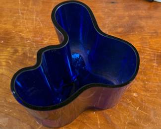 This lot features a Iittala Alvar Aalto Collection vase in ultramarine blue mouth-blown glass. It is also known as the Savoy Vase. The vase was designed by Finnish architect Alvar Aalto and his wife Aino for a design competition in 1936. It became an iconic piece of Finnish design after being displayed at the 1937 Paris World’s Fair. The unique, wavy shape was reportedly inspired by the hem of a Sami woman’s dress, with original sketches titled “The Eskimo Woman’s Leather Breeches”. Each vase is still manufactured by skilled glassblowers at the Iittala factory in Finland using original wooden molds. This vase is accompanied with Aalto’s MOMA book.


