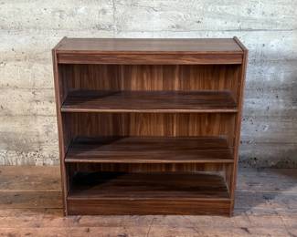 This lot features a three-shelf bookcase with a walnut veneer that measures, 36” H x 36” W x 12” D.


