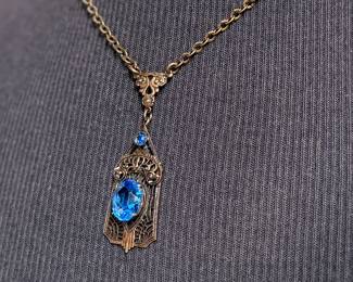 This lot features an antique Art Deco sterling silver filigree pendant necklace with a large blue central stone, likely blue chalcedony or glass, and marcasite accents. The intricate filigree design and geometric patterns are characteristic of the Art Deco period, circa the 1920s-1930s. This necklace measures, 18”.

