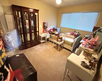 This room is packed with dolls, twin size bedroom furniture, antique trunk, large curio/display cabinet and pillows.