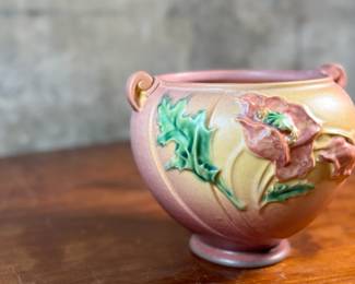 This lot features a Roseville Poppy jardiniere (or vase/planter) in very good condition. The Poppy line of art pottery was introduced by Roseville in 1938. It features raised poppy flowers and buds in a mauve or pink color with vivid green leaves against a shaded background. This vase measures, 6” H x 7.5” W x 7” D.

