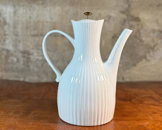 This lot features a vintage Ernest Sohn Creations "Doric" line white ribbed ceramic coffee server or teapot. It was designed by Ernest Sohn and produced by Hall China in the 1950s. This model typically holds around 10 to 12 cups of coffee or tea and measures, 12” H x 10” W x 6” D.

