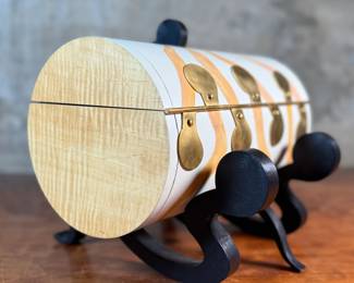 This lot features an original work of art by listed artist, Garry Knox Bennett. This piece is a uniquely designed humidor, signed by Bennett underneath circa 1997. This piece measures, 10” H x 11” W x 9” D. Born in Alameda, California, Garry Knox Bennett is a self-taught studio furniture maker who uses traditional fine woodworking techniques for both synthetic and natural materials. He attended the California College of Arts and Crafts in Oakland from 1959 to 1962 and then worked as a metal sculptor.

