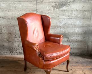 This lot features a Georgian-style leather wingback armchair in a warm, caramel or reddish-brown cowhide leather that measures, 42” H x 32” W x 27” D.

