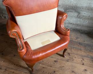 This lot features a Georgian-style leather wingback armchair in a warm, caramel or reddish-brown cowhide leather that measures, 42” H x 32” W x 27” D.

