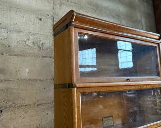 This lot features a stacking barrister bookcase manufactured by Globe Wernicke, dating back to the early 1900s. This bookcase in particular has a total of eight (8) pieces – 6 stacking bookcases, a base, and a topper. This piece measures from top to bottom, 90” H x 34” W x 11” D.

