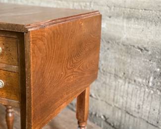 This lot features an antique drop-leaf side table with two dove-tailed drawers. This table measures (closed), 28.5” H x 19.5” W x 20.75” and each leaf adds an additional 11” of width. 

