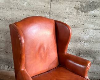 This lot features a Georgian-style leather wingback armchair in a warm, caramel or reddish-brown cowhide leather that measures, 42” H x 32” W x 27” D.

