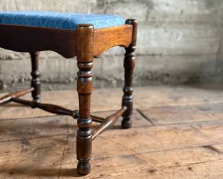 This lot features an antique English oak upholstered joint stool with turned legs and stretchers that measures, 16” H x 18” W x 13.5” D.


