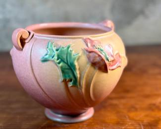 This lot features a Roseville Poppy jardiniere (or vase/planter) in very good condition. The Poppy line of art pottery was introduced by Roseville in 1938. It features raised poppy flowers and buds in a mauve or pink color with vivid green leaves against a shaded background. This vase measures, 6” H x 7.5” W x 7” D.

