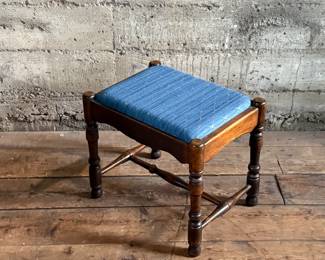 This lot features an antique English oak upholstered joint stool with turned legs and stretchers that measures, 16” H x 18” W x 13.5” D.

