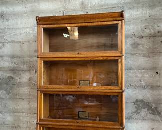 This lot features a stacking barrister bookcase manufactured by Globe Wernicke, dating back to the early 1900s. This bookcase in particular has a total of eight (8) pieces – 6 stacking bookcases, a base, and a topper. This piece measures from top to bottom, 90” H x 34” W x 11” D.

