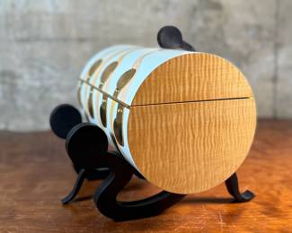 This lot features an original work of art by listed artist, Garry Knox Bennett. This piece is a uniquely designed humidor, signed by Bennett underneath circa 1997. This piece measures, 10” H x 11” W x 9” D. Born in Alameda, California, Garry Knox Bennett is a self-taught studio furniture maker who uses traditional fine woodworking techniques for both synthetic and natural materials. He attended the California College of Arts and Crafts in Oakland from 1959 to 1962 and then worked as a metal sculptor.

