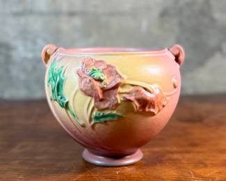 This lot features a Roseville Poppy jardiniere (or vase/planter) in very good condition. The Poppy line of art pottery was introduced by Roseville in 1938. It features raised poppy flowers and buds in a mauve or pink color with vivid green leaves against a shaded background. This vase measures, 6” H x 7.5” W x 7” D.

