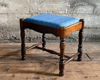 This lot features an antique English oak upholstered joint stool with turned legs and stretchers that measures, 16” H x 18” W x 13.5” D.

