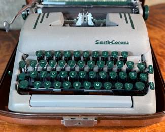 This lot features a vintage Smith Corona Silent-Super portable typewriter, circa 1950s. It has a khaki-toned body and forest green keys, and is shown with its original carrying case. 

