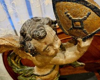 This is a pair of 18th-century Italian carved wooden cherubs.
They are hand-carved from wood and feature a parcel- painted finish with gold accents.
The cherubs present as reflections of each other with one holding a shield and the other a horn-like object.