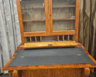 Secretary Desk 
72.75” tall, 43.5” wide, 24” deep, 32” deep (desk open)
Tiger Maple. Attributed to Biedermeir style, American made Classical Revival Style
A rectangular Secretary Writing Desk with fold out writing surface below 
Glass enclosed shelves and architectural cornice raised on curved legs supporting lower cupboard and drawer with key.   1830-1845