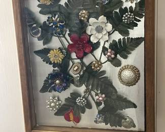 Rosenberg Estate Sale on 01/24/2025 featuring a decorative picture frame accented with brooches. A unique display piece combining vintage jewelry with functional décor.