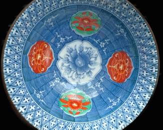 Japanese Arita ware porcelain bowl  produced by the Juzan Gama family kiln.  . It features a hand-painted design in the traditional blue-and-white style (known as sometsuke in Japan), augmented with overglaze orange/red flowers (peony or chrysanthemum motifs) and green leaves, a style often associated with Imari ware. This specific pattern with the blue crosshatch rim is characteristic of the kiln's output during the mid-to-late 20th century (Showa period). 