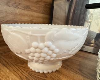 This is an L.E. Smith or Westmoreland White Milk Glass Grape & Leaves Pedestal Compote. 
It features a decorative "Paneled Grape" cluster and leaf design with scalloped edges. The item is made of white milk glass and has a footed base.