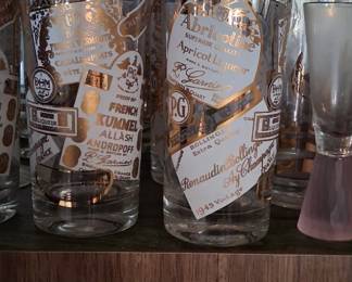 vintage gilt tumblers featuring a pattern of liquor labels, often referred to as MCM (Mid-Century Modern) barware