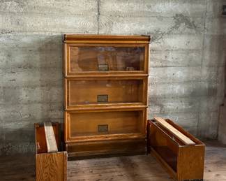 This lot features a stacking barrister bookcase manufactured by Globe Wernicke, dating back to the early 1900s. This bookcase in particular has a total of five (5) pieces – 3 stacking bookcases, a base, and a topper. This piece measures from top to bottom, 49.5” H x 34” W x 11” D. This lot also includes two (2) additional stacking bookcases that are missing the glass to be used as is or repaired.

