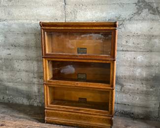 This lot features a stacking barrister bookcase manufactured by Globe Wernicke, dating back to the early 1900s. This bookcase in particular has a total of five (5) pieces – 3 stacking bookcases, a base, and a topper. This piece measures from top to bottom, 49.5” H x 34” W x 11” D.

