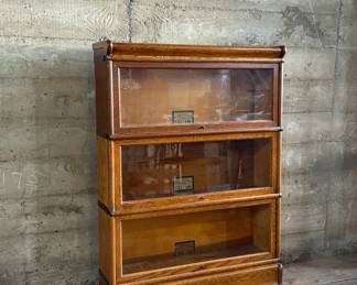This lot features a stacking barrister bookcase manufactured by Globe Wernicke, dating back to the early 1900s. This bookcase in particular has a total of five (5) pieces – 3 stacking bookcases, a base, and a topper. This piece measures from top to bottom, 49.5” H x 34” W x 11” D.

