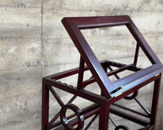 This lot features a library book stand, made of teak with a mahogany finish. This stand measures, 40.5” H x 20” W x 14” D.  The simple neoclassical fretwork on the sides and back gives it great visual distinction. Wide glass shelves provide ample storage, with a special tilting shelf on top for an atlas, dictionary or other frequently consulted volumes. All glass inserts included (not photographed).

