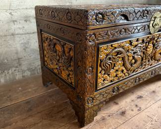 This lot features a Chinese hand-carved camphor wood chest. The chest is made of camphor wood, which is naturally moth-resistant, making it a practical storage solution for clothing or blankets. It features intricate carvings, including dragon panels surrounded by floral or cloud motifs, common in Chinese design. This chest measures, 22.5” H x 39.5” W x 21” D.

