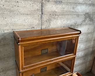 This lot features a stacking barrister bookcase manufactured by Globe Wernicke, dating back to the early 1900s. This bookcase in particular has a total of five (5) pieces – 3 stacking bookcases, a base, and a topper. This piece measures from top to bottom, 49.5” H x 34” W x 11” D. This lot also includes two (2) additional stacking bookcases that are missing the glass to be used as is or repaired.

