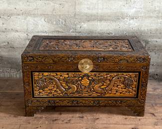 This lot features a Chinese hand-carved camphor wood chest. The chest is made of camphor wood, which is naturally moth-resistant, making it a practical storage solution for clothing or blankets. It features intricate carvings, including dragon panels surrounded by floral or cloud motifs, common in Chinese design. This chest measures, 22.5” H x 39.5” W x 21” D.

