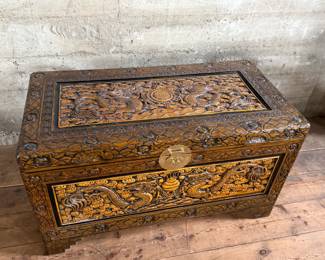 This lot features a Chinese hand-carved camphor wood chest. The chest is made of camphor wood, which is naturally moth-resistant, making it a practical storage solution for clothing or blankets. It features intricate carvings, including dragon panels surrounded by floral or cloud motifs, common in Chinese design. This chest measures, 22.5” H x 39.5” W x 21” D.

