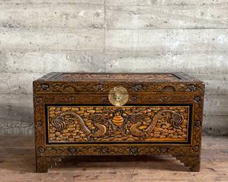 This lot features a Chinese hand-carved camphor wood chest. The chest is made of camphor wood, which is naturally moth-resistant, making it a practical storage solution for clothing or blankets. It features intricate carvings, including dragon panels surrounded by floral or cloud motifs, common in Chinese design. This chest measures, 22.5” H x 39.5” W x 21” D.

