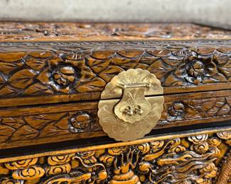 This lot features a Chinese hand-carved camphor wood chest. The chest is made of camphor wood, which is naturally moth-resistant, making it a practical storage solution for clothing or blankets. It features intricate carvings, including dragon panels surrounded by floral or cloud motifs, common in Chinese design. This chest measures, 22.5” H x 39.5” W x 21” D.

