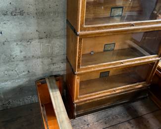 This lot features a stacking barrister bookcase manufactured by Globe Wernicke, dating back to the early 1900s. This bookcase in particular has a total of five (5) pieces – 3 stacking bookcases, a base, and a topper. This piece measures from top to bottom, 49.5” H x 34” W x 11” D. This lot also includes two (2) additional stacking bookcases that are missing the glass to be used as is or repaired.

