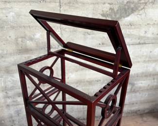This lot features a library book stand, made of teak with a mahogany finish. This stand measures, 40.5” H x 20” W x 14” D.  The simple neoclassical fretwork on the sides and back gives it great visual distinction. Wide glass shelves provide ample storage, with a special tilting shelf on top for an atlas, dictionary or other frequently consulted volumes. All glass inserts included (not photographed).

