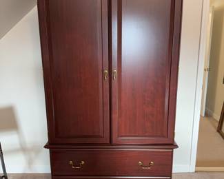 Cherry finish armoire with adjustable shelves and two large drawers.